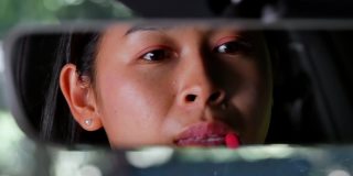 在停车场，一个美丽的女人一边画嘴唇一边看着汽车后视镜，一边看着汽车的整洁，然后下车为面试做准备。工作应用程序的概念。