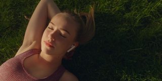 放松的女人戴着耳机欣赏音乐，闭着眼睛躺在草地上