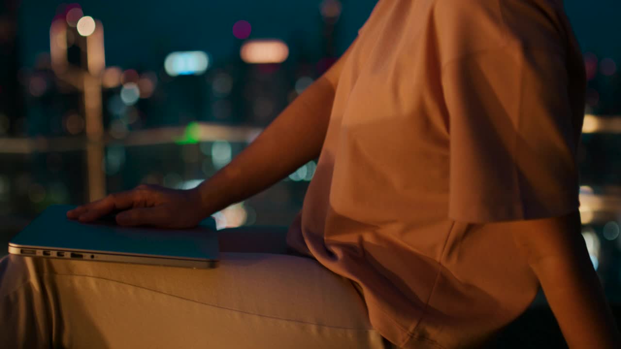 一个年轻女人的手在城市之夜用笔记本电脑