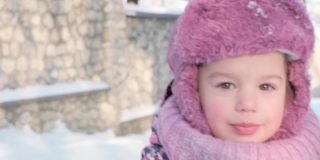 冬天，假期，游戏，家庭概念-慢动作特写，真实的3-4岁的小学前班小女孩穿着紫色的衣服看着镜头用舌头舔着雪上的冰凌。孩子在雪地上奔跑
