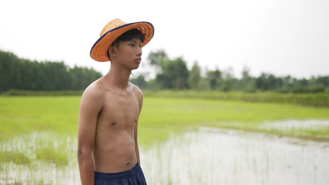 年轻的农民赤膊站在稻田里，双臂交叉