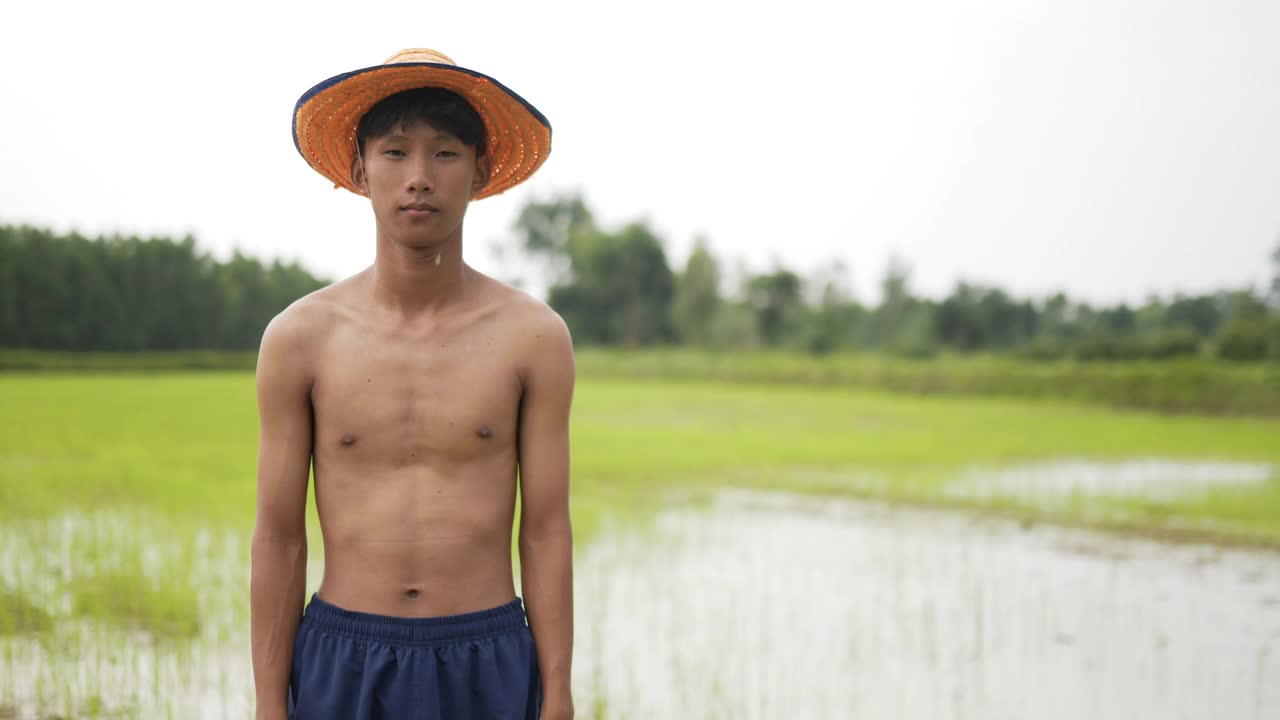 年轻的农民赤膊站在稻田里，双臂交叉