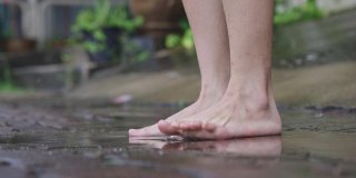 雨后活动，闭上赤脚在水坑里慢慢跺脚，铺在一条水泥小路上，热带雨季，气候变化，环境问题，成人玩水嬉戏