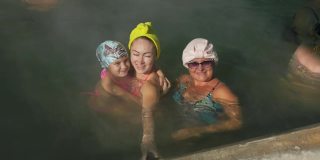 宝贝女儿，妈妈和奶奶在一个传统的户外温泉温泉与柔和的灯光蒸汽热盐水浴。女孩女人放松。