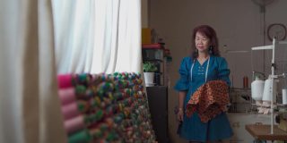亚洲华人高级女性裁缝在工作室工作室选择丝线搭配面料服装