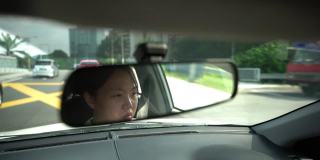 一位亚裔中国妇女坐在驾驶座上，在城市道路上开车