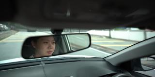 一位亚裔中国妇女坐在驾驶座上，在城市道路上开车