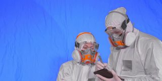 呼吸器中的科学家病毒学家用手写笔在平板电脑中书写。男男女女都戴着医用防护口罩色度键蓝色。