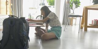 亚洲女孩一边做作业一边在家学习在线课程，社交距离的生活方式概念。