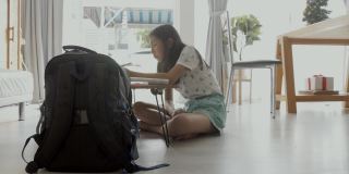 亚洲女孩一边做作业一边在家学习在线课程，社交距离的生活方式概念。