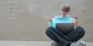 年轻的女博主坐在城市户外的一台笔记本电脑显示器前。她在在线视频通话时主动做手势