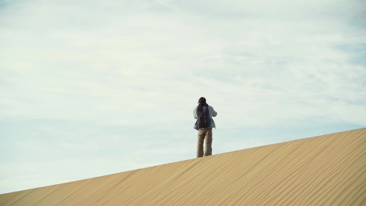 一个亚洲人在多云的天空下走在沙丘上