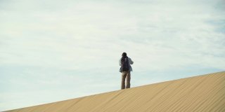 一个亚洲人在多云的天空下走在沙丘上