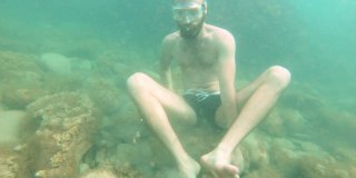 一个长着胡子的年轻男子在海底慢慢地移动，试图以莲花的姿势冥想。禅宗冥想和水下瑜伽的概念