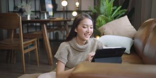 一名亚洲女性在家里开心地用平板电脑看喜剧