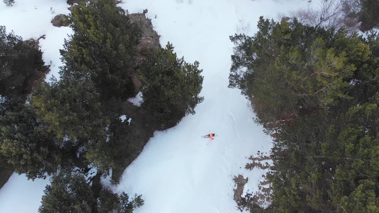 鸟瞰图，一名身穿橙色服装的滑雪者骑下残留在春季森林中的雪。春季极限滑雪