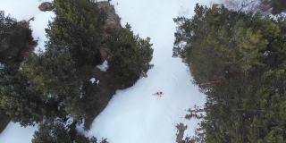 鸟瞰图，一名身穿橙色服装的滑雪者骑下残留在春季森林中的雪。春季极限滑雪