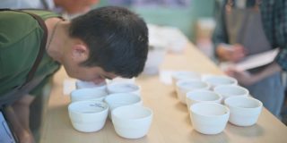 专业的亚洲华人咖啡师，鉴赏家，评分员，表演咖啡杯和他的同事品尝咖啡杯后写在剪贴板上