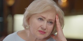 特写肖像悲伤的皱纹白人妇女头痛偏头痛触摸太阳穴和前额。女退休人员的大头照在家里，脸上带着痛苦的疼痛和不安的表情。老化