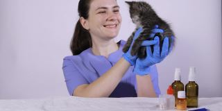 一位身穿蓝色制服的女兽医抱着一只灰色的小猫，微笑着对一只生病的猫说话。