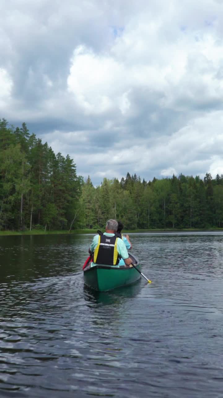 一对成熟的夫妇在芬兰的森林湖上划独木舟。一个垂直方向的视频