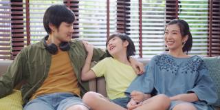 亚洲家庭坐着放松与儿子积极交谈，幸福微笑的男孩与父母随意交谈，快乐的亚洲家庭一起在沙发上享受假期，家温馨的家客厅