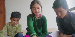 一个小女孩正在教一群印度亚裔小学的孩子们在室内用笔记本电脑一起学习