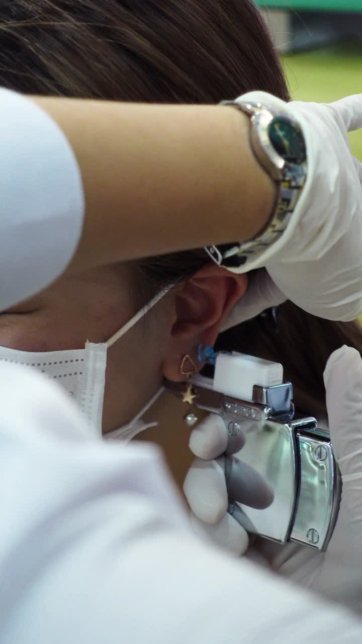 一个十几岁的女孩在美容院做耳洞手术后检查她的耳朵
