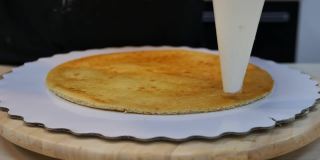 一个糕点袋把白奶油挤在一个薄薄的海绵蛋糕上，形成一个圆圈