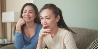 千禧一代的亚洲女性朋友们一起在家里的客厅里看电视。
