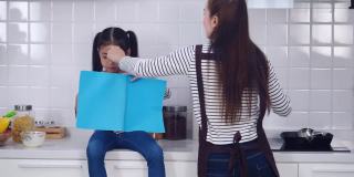 小亚洲女孩一边看书，一边等妈妈在家里厨房做饭。
