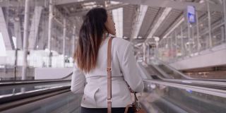 女商人在机场往前走，亚洲女商人，在机场做生意带着行李和肩袋在自动扶梯上，手持后视镜