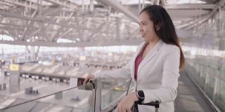 女商人在机场往前走，亚洲女商人，带着行李和背包在机场出差时用智能手机和同事讨论，感受新旅程的积极情绪，手持侧视
