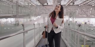 女商人在机场往前走，亚洲女商人，带着行李、背包和笔记本电脑，在机场步行去上班，感受新旅程的积极情绪，手持大头照正面