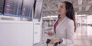 女商人在机场沟通预订航班，亚洲女商人，检查航班的时间，使她的商务旅行在屏幕上看到航班号，使用电话做生意，在国外工作