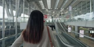 亚洲女性旅客在机场带着行李，护照，机票，一个新的旅程，旅行，度假在自动扶梯上，后面的视图