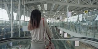์ื新常态od亚洲女性旅客在机场身穿粉色t恤，携带行李、护照和机票，戴着防COVID-19口罩，踏上新的旅程，旅行，度假，在自动扶梯上，后视镜