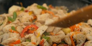 厨师在煎锅里把鸡肉和蔬菜混合起来。专业厨师在锅里准备蔬菜鸡肉。多汁的鸡排和新鲜的蔬菜一起在锅里炸