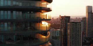 向上拍摄的高大的现代圆形公寓大楼，周围有一圈露台。夕阳映照下的城市景观。英国伦敦