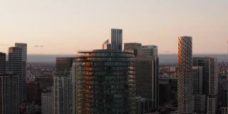 巴尔的摩塔顶部的幻灯片和平移镜头。圆柱形公寓建筑，周围有露台。金丝雀码头区的摩天大楼和日落时的城市景观。英国伦敦