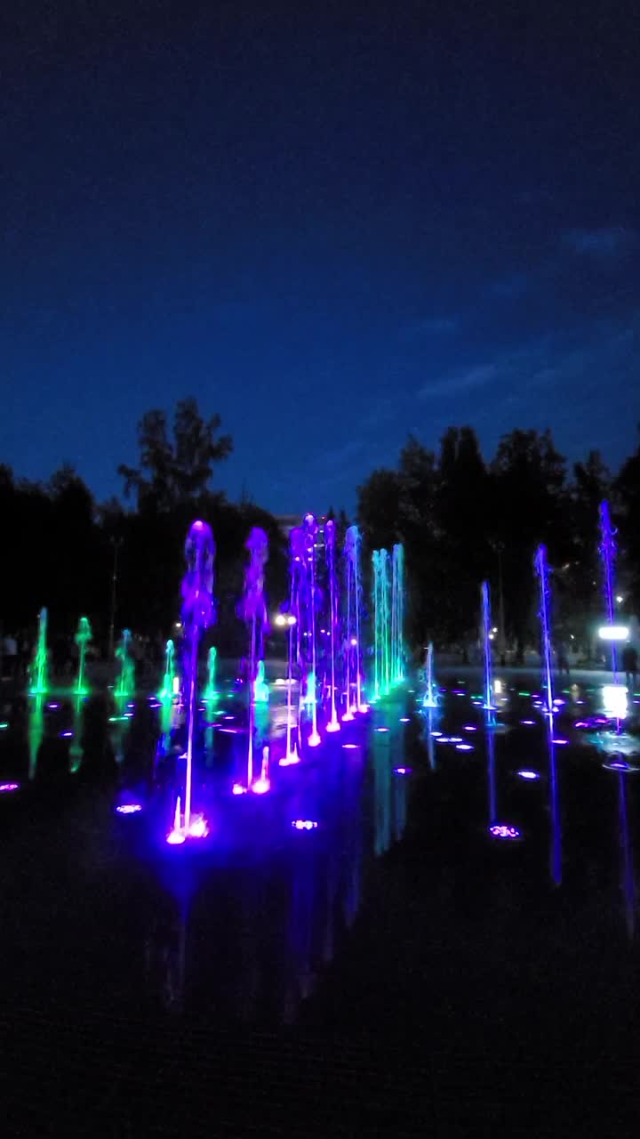 五彩缤纷的灯光音乐舞蹈城市喷泉。喷泉的碎片。明确多彩水。以公园为背景。晚上的时间。垂直新西伯利亚