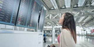 一名亚洲女性旅客在机场，看着她旅行的航班带着行李，在显示器屏幕上看到航班号去新旅行，旅行度假，侧视