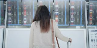 一名亚洲女性旅客在机场，看着她旅行的航班带着行李，在屏幕上看到航班号，就开始了新的旅行，旅行度假，后视镜