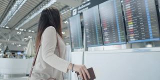一名亚洲女性旅客在机场，看着她旅行的航班带着行李，在屏幕上看到航班号就开始了新的旅行，旅行度假