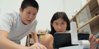 亚洲男孩教女孩在家用智能手机和无线键盘玩网络游戏，生活理念。