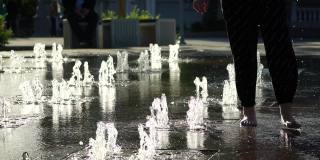 干涸的城市喷泉，水的喷射高度变化，没有碗。炎炎夏日日落时的城市景象。孩子们在喷泉边上玩耍。慢动作，选择性聚焦。近距离