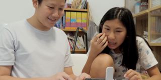 亚洲男孩教女孩在家用智能手机和无线键盘玩网络游戏，生活理念。