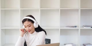 亚洲女性戴着耳机在笔记本电脑上听音乐。放松的时间。