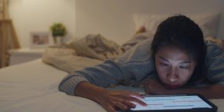 自由亚洲妇女休闲穿着使用笔记本电脑努力工作在床上在卧室在家里晚上。
