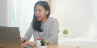 年轻的亚洲女商人使用笔记本电脑与同事在视频通话计划，同时在卧室智能工作。